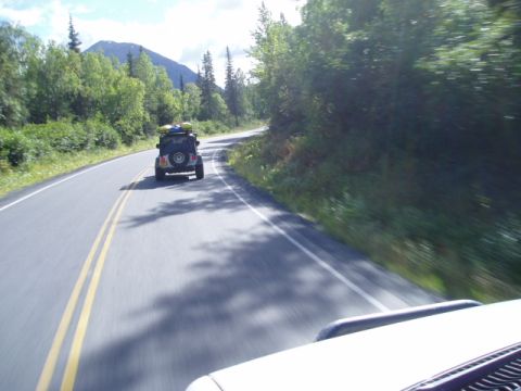 2000 Ford E350 - Two vehicles travel down a scenic highway surrounded by lush green trees and a mountain in the distance.