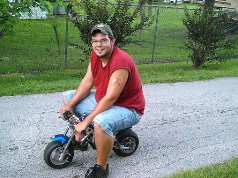 1986 Ford Bronco - A man rides a small blue motorcycle on a paved road outdoors.