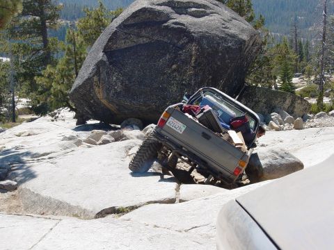 1986 Ford Bronco - An off-road vehicle navigates a challenging rocky terrain, with a large boulder nearby.
