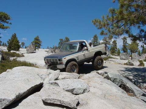 1986 Ford Bronco - This lifted 1986 Ford Bronco navigates a rocky trail under a clear blue sky.