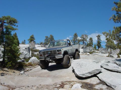 1986 Ford Bronco - Pickup truck off-roading on a sunny day with a clear blue sky.