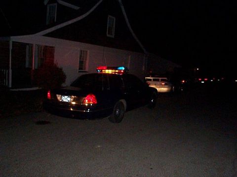 1991 Ford Crown Victoria - A police car with its light bar illuminated sits parked at night, with another vehicle visible in the distance.