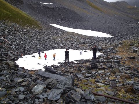 2000 Ford E350 - People explore a rocky mountain terrain with patches of snow and sparse vegetation.