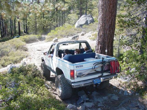 1986 Ford Bronco - This 1986 Ford Bronco is navigating a challenging off-road trail surrounded by trees and rocks.
