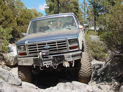 1986 Ford Bronco - This modified Ford Bronco is tackling a challenging off-road course with large tires and a winch.