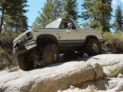 1986 Ford Bronco - This modified Ford Bronco navigates a rocky trail under a clear blue sky.