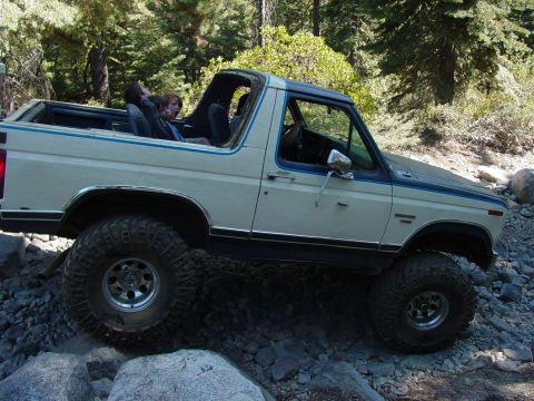 1986 Ford Bronco - White Ford Bronco with blue trim navigates a rocky trail with passengers in the rear.