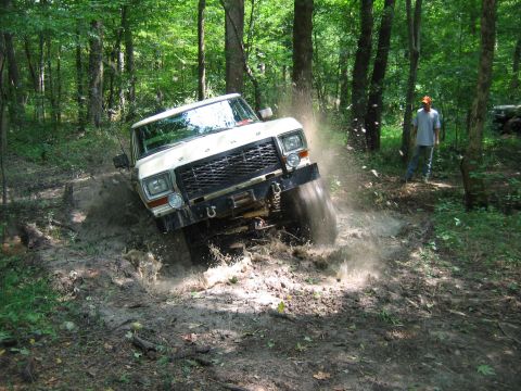 1992 Ford Mustang - A white 1980s Ford Bronco navigates a muddy trail, kicking up water and dirt. Another vehicle can be seen in the background.