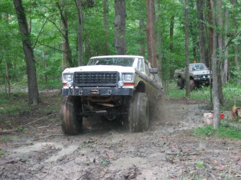 1992 Ford Mustang - A lifted pickup truck navigates a muddy trail in a forest, with another vehicle in the background.