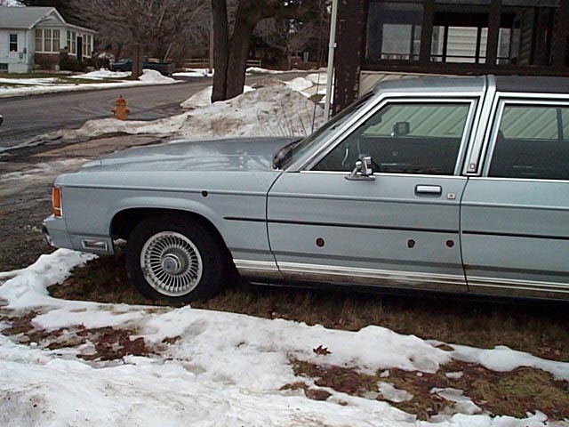 Light blue 1980s Ford LTD Crown Victoria sedan in side view on a snowy street