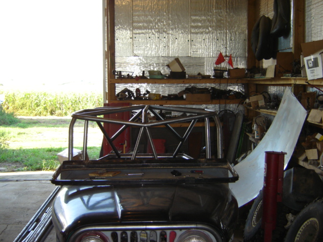 Roll cage assembly on top of a dark-colored vehicle's hood inside a garage