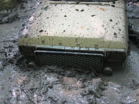 1992 Ford Mustang - A vintage Ford Mustang is stuck deep in the mud, with only its front grille and headlights visible.