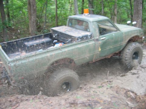 1992 Ford Mustang - A green pickup truck is stuck in thick mud, with its tires partially submerged and mud splashing around.
