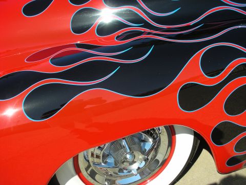 1998 Ford Crown Victoria - Close-up of glossy black bodywork with red flame paint outlined in blue, curling over a chrome wheel and whitewall tire.