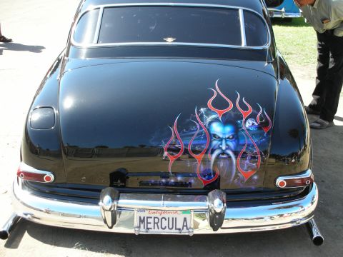 1998 Ford Crown Victoria - trunk of a black custom car carries an airbrushed blue demon face surrounded by red flames above a California MERCULA plate.