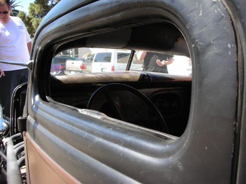 1998 Ford Crown Victoria - Looking through the open side window of a weathered black rat-rod cab reveals the steering wheel and bare dashboard inside.