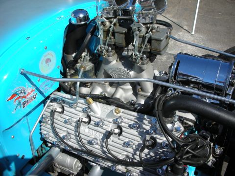 1998 Ford Crown Victoria - polished V8 engine with multiple carburetors, finned valve covers, and a teal firewall fills the engine bay of a hot rod.