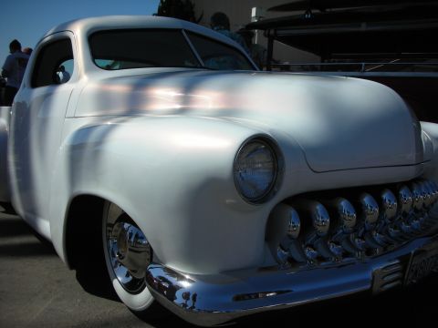 1998 Ford Crown Victoria - white chopped custom coupe with a frenched headlight and a prominent toothy chrome grille sits in the sun at a car show.