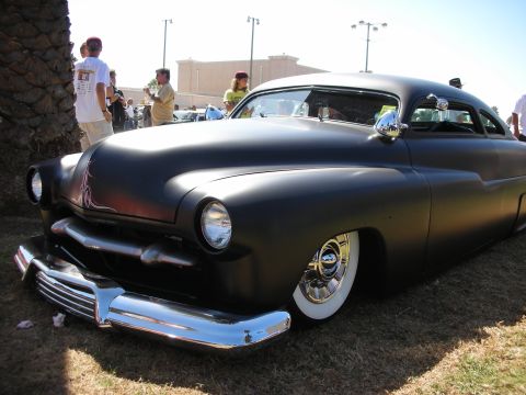 1998 Ford Crown Victoria - flat-black chopped custom coupe with faint flame fade, whitewall tires and chrome bumper sits on grass at a sunny car show.