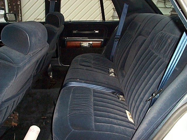 Navy blue velour rear bench seat of a full-size sedan seen through the open door