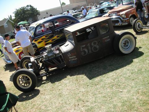 1998 Ford Crown Victoria - chopped flame-painted rat rod sedan marked 518 with exposed front engine and yellow wheels parked among hot rods at a show.