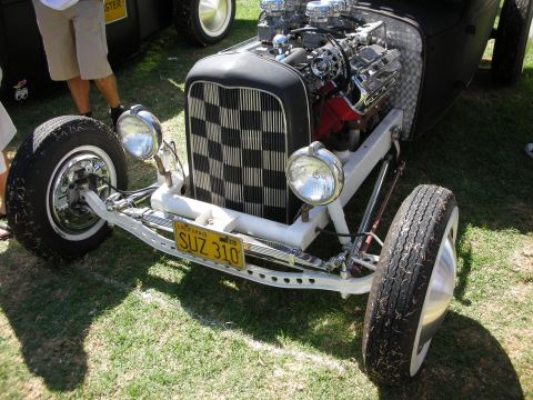 1998 Ford Crown Victoria - black hot rod roadster with a checkerboard grille insert, exposed blown engine, white frame and yellow plate SUZ 310 on grass.