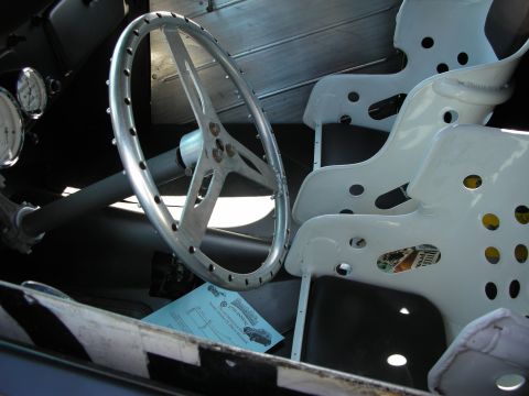 1998 Ford Crown Victoria - Interior of a stripped hot rod showing a polished three-spoke steering wheel and white lightening-drilled seat frames with a paper note.
