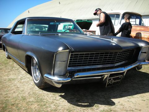 1998 Ford Crown Victoria - flat-black Buick Riviera with clamshell headlights and chrome bumper shown front three-quarter on grass, with a Riviera badge on the bumper.