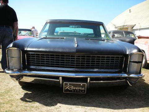1998 Ford Crown Victoria - Head-on view of a flat-black Buick Riviera showing its wide horizontal grille, hidden headlights and a Riviera by Buick front plate.