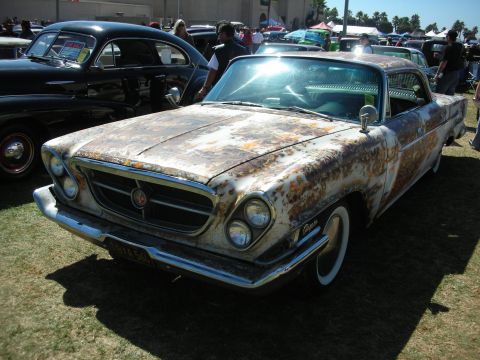 1998 Ford Crown Victoria - heavily rust-patinated early-1960s coupe with dual headlights, split grille and whitewall tires parked on grass among other cars.