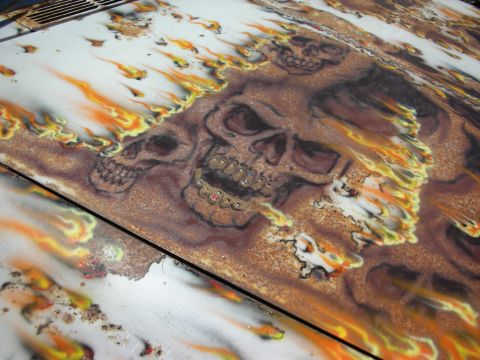 1998 Ford Crown Victoria - Close-up of airbrushed artwork showing grinning skulls amid orange and yellow flames over a rust-textured surface.