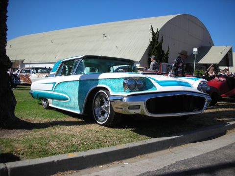 1998 Ford Crown Victoria - white custom coupe with turquoise metalflake panels and quad headlights shown front three-quarter on grass beside a domed hangar building.