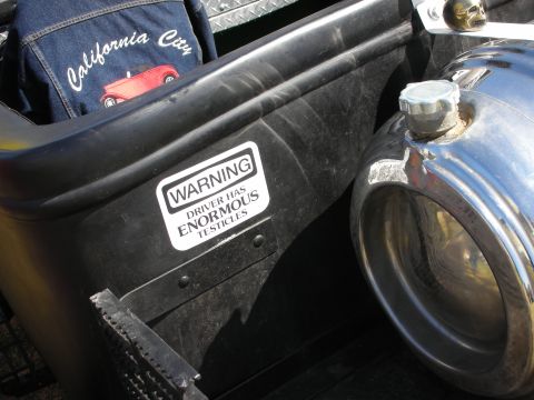 1998 Ford Crown Victoria - Detail of a black hot rod's rear showing a chrome exhaust tip, a quilted seat and a novelty WARNING sticker about the driver.