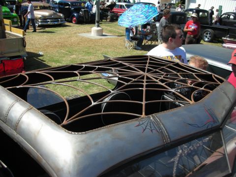 1998 Ford Crown Victoria - bare-metal custom car with its roof replaced by a fabricated steel spider-web panel, with a spiderweb pinstripe on the quarter, at a show.