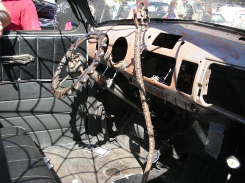1998 Ford Crown Victoria - Stripped interior of a rat rod showing a bare rusted steel dash, exposed wiring and a spider-web themed shifter at a car show.