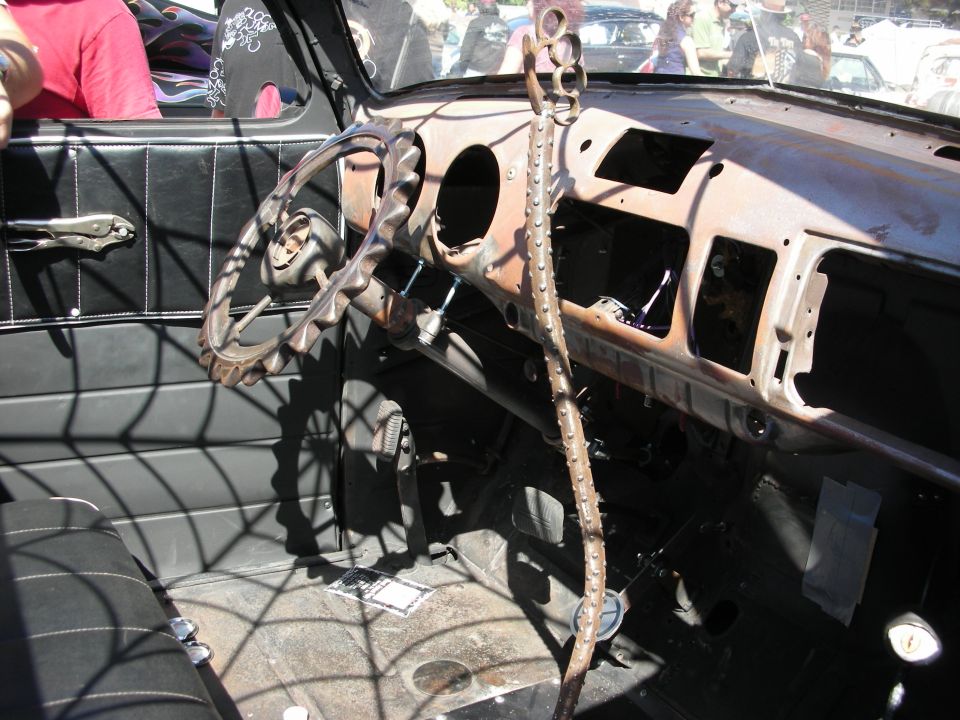 Bare rusty steel dashboard of a hot rod with spider-web details and stick shifter