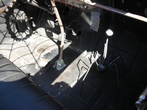 1998 Ford Crown Victoria - Sunlit bare-metal floor and gearshift of a stripped rat rod interior with spider-web themed metal accents.