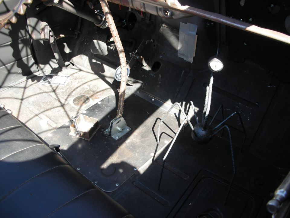 Bare metal floorpan and shifter area inside a stripped hot rod with spider-web decor