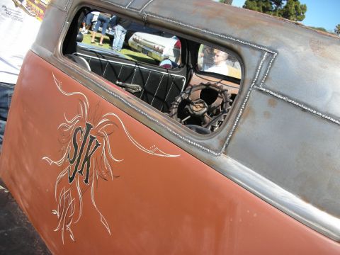 1998 Ford Crown Victoria - Side window and door of a rat rod showing rust patina, bare steel roof and white pinstriped lettering reading SK.