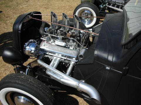 1998 Ford Crown Victoria - Polished V8 engine with multiple carburetors and chrome zoomie exhaust mounted in a black hot rod with whitewall tires.
