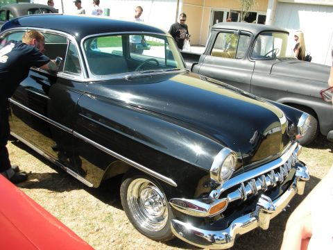 1998 Ford Crown Victoria - Lowered glossy black mid-1950s Chevrolet two-door being detailed by a man, with a patina pickup and other cars behind.