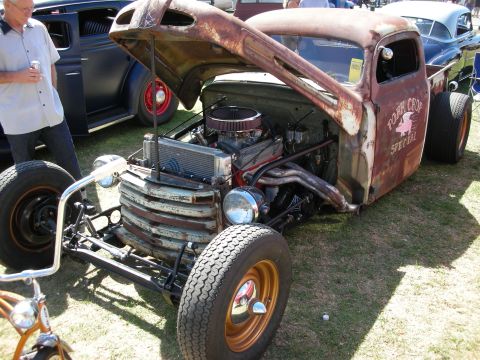 1998 Ford Crown Victoria - Channeled rat rod pickup with heavy rust patina, exposed chrome V8 and gold wheels marked Pork Chop Special on the door.