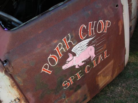 1998 Ford Crown Victoria - Close-up of a rusty patina door with hand-painted winged pig artwork and the words Pork Chop Special.