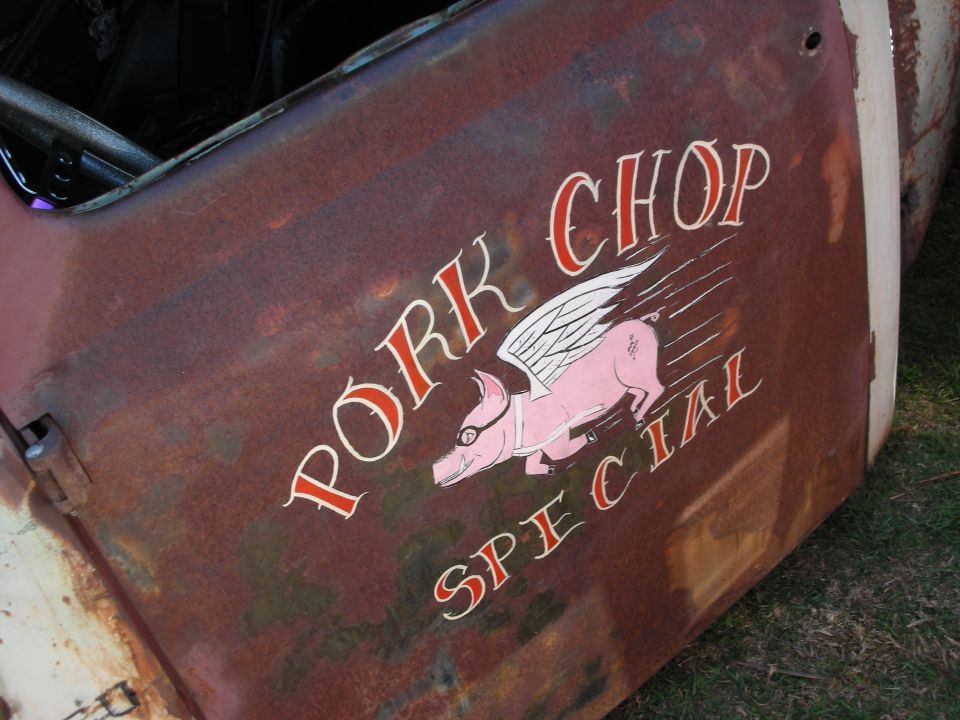 Rusty truck door painted with a winged flying pig and 'Pork Chop Special' text