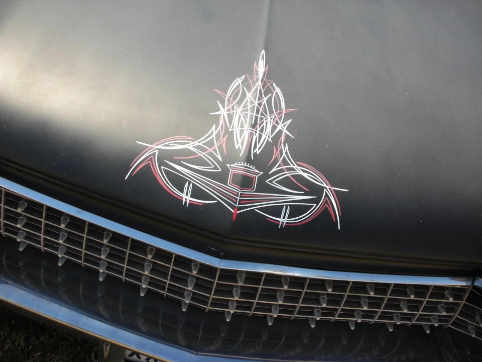 Matte black car hood with red and white pinstripe artwork above a chrome grille