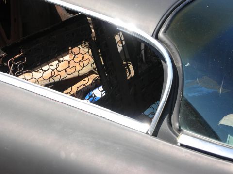 1998 Ford Crown Victoria - Through the open window of a gray rat rod, exposed chain-link and metal cab framing is visible in sunlight.