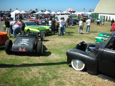 1998 Ford Crown Victoria - Wide view of an outdoor hot rod show on grass with parked rat rods, custom cars, crowds, vendor tents and a carnival tent.