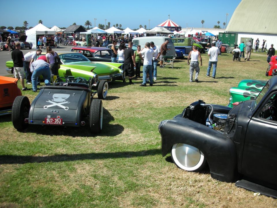 Outdoor hot rod and rat rod show on grass with crowds, tents and a carnival ride