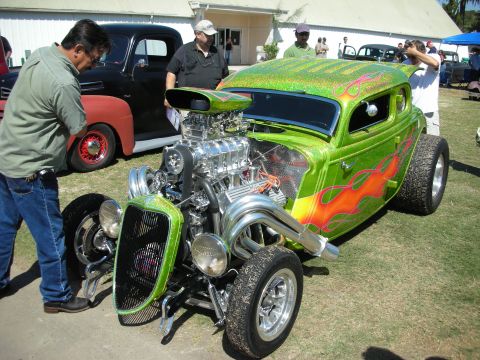1998 Ford Crown Victoria - Bright green flamed 1930s Ford coupe hot rod with a chrome blower-topped V8 and chopped top, drawing onlookers at a show.