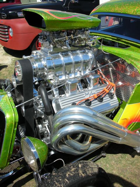 1998 Ford Crown Victoria - Vertical view of a green metalflake hot rod's exposed blown V8 with bug-catcher injection and chrome headers in sunlight.